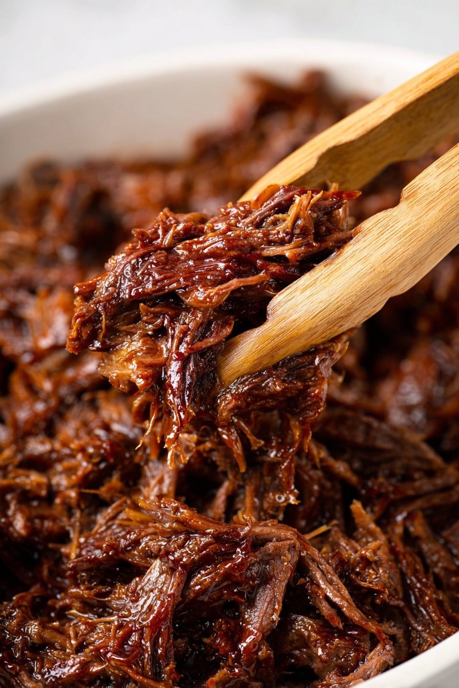 The image shows a close-up of a wooden tong holding a portion of shredded meat that looks juicy and tender. The meat is dark brown with a glossy texture, showing small strands and fibers. The background is filled with more shredded meat, all resting in a white dish with a smooth surface. The photo is bright and detailed, highlighting the moist and well-cooked texture of the meat. photo taken with an iphone --ar 2:3 --v 7