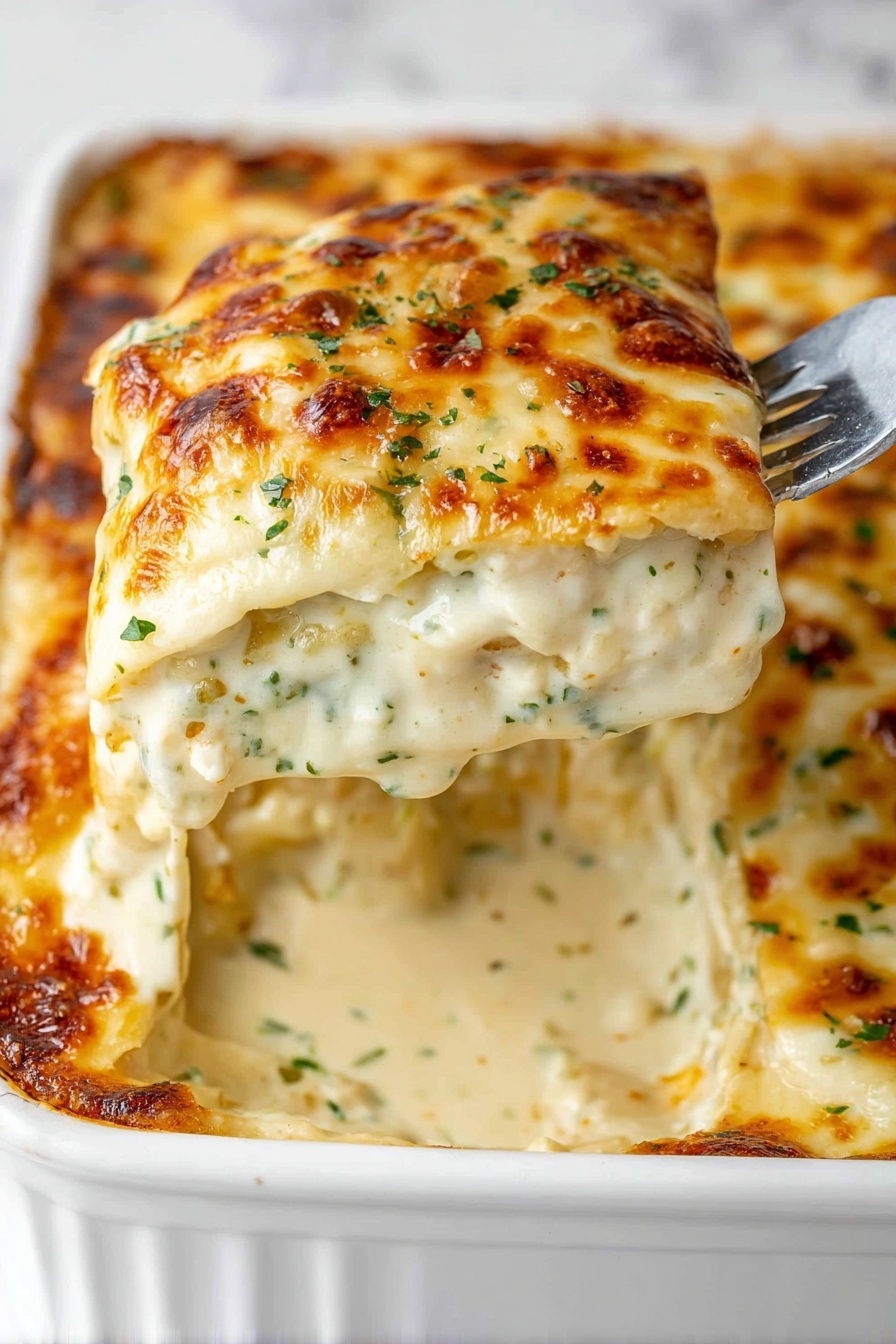 This dish shows a thick slice of creamy, cheesy casserole lifted on a fork above a white baking dish. The casserole has three visible layers: the top is a golden-brown, bubbly melted cheese with small green herbs sprinkled on it; beneath is a thick, white creamy sauce speckled with herbs and spices; the base layer looks like soft pasta sheets covered in sauce. The casserole is gooey with melted cheese stretching slightly from the fork. The white baking dish has a ridged edge and the background is a white marbled texture. Photo taken with an iphone --ar 2:3 --v 7