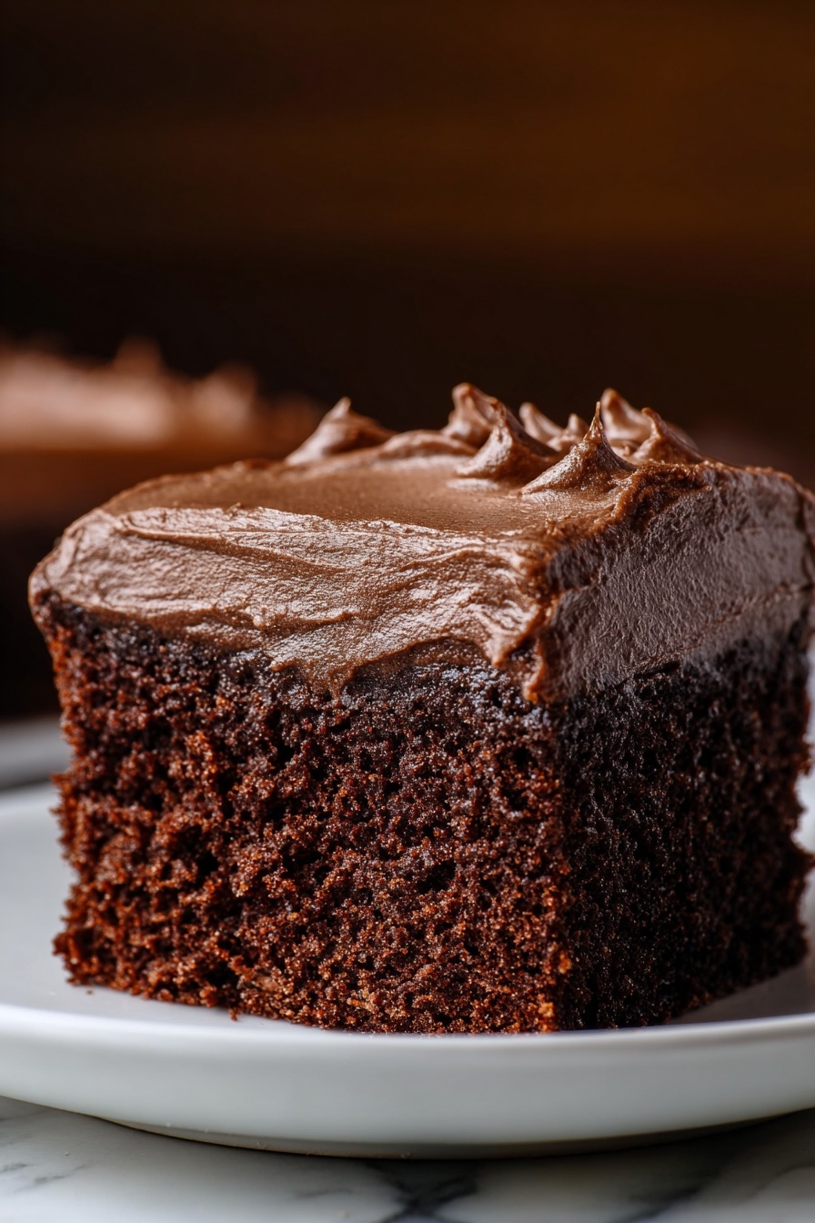 A close-up image of a single square piece of chocolate cake on a white plate, placed on a white marbled surface. The cake has two layers: the bottom layer is thick, moist, and dark brown chocolate sponge with a crumbly texture, while the top layer is a smooth, thick, rich chocolate frosting with slight swirls and soft peaks. The background is softly blurred in warm brown tones, focusing all attention on the cake itself. Photo taken with an iphone --ar 2:3 --v 7