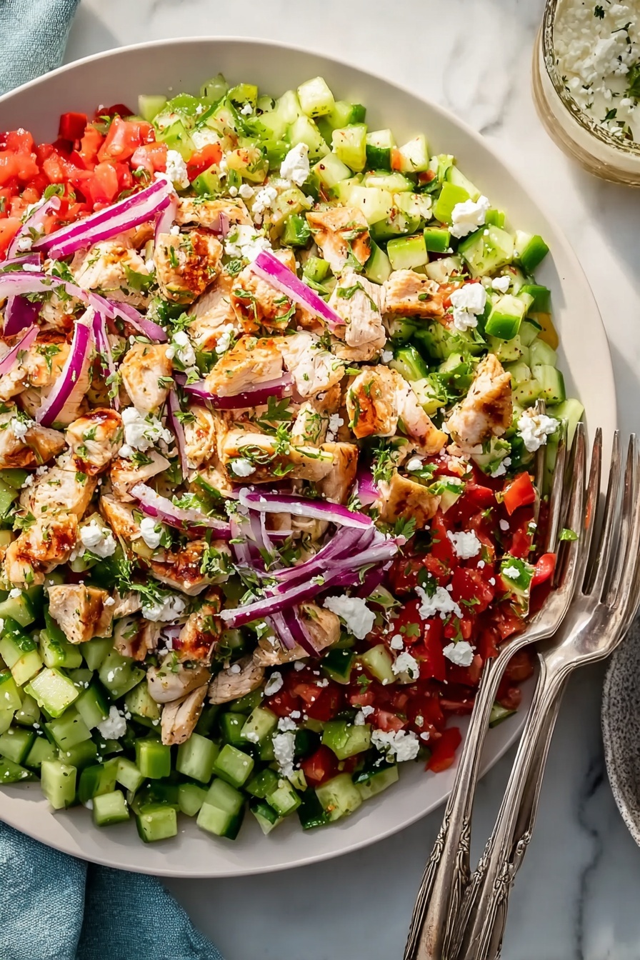 A large, shallow light blue plate holds a colorful salad with multiple layers. The bottom layer has bright green cucumber pieces and chopped red tomatoes mixed with small bits of green bell pepper. On top, there are light purple thin slices of onion spread evenly. Scattered over the salad are medium-sized chunks of cooked light brown chicken. White crumbles of cheese are sprinkled on the very top, adding a soft texture. Two silver forks rest on the right edge of the plate. The plate is placed on a white marbled surface, with a piece of pita bread on a white plate just visible on the right side. Photo taken with an iphone --ar 2:3 --v 7