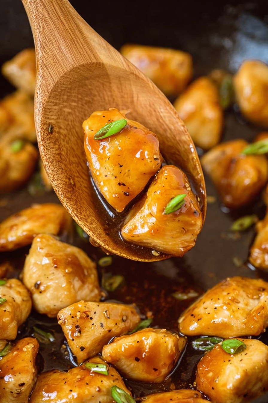 The image shows many golden brown chicken pieces with a shiny glaze in a black pan, with a wooden spoon lifting two pieces along with a small slice of green onion. The chicken pieces are cooked evenly with a slight char and coated in a glossy, sticky brown sauce. Small green onion slices are scattered among the chicken, adding a touch of green color. The background is a white marbled texture. photo taken with an iphone --ar 2:3 --v 7