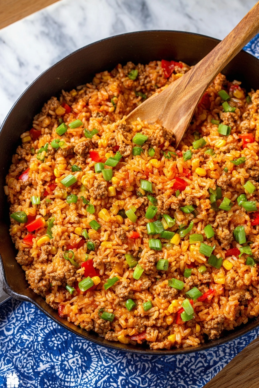 A close-up view of a large black pan filled with a one-layer rice dish mixed with brown cooked ground meat, yellow corn kernels, small red and green bell pepper chunks, and sprinkled green onions on top. A wooden spoon is scooping the colorful mixture from the pan, which rests on a blue and white patterned cloth over a white marbled surface. photo taken with an iphone --ar 2:3 --v 7