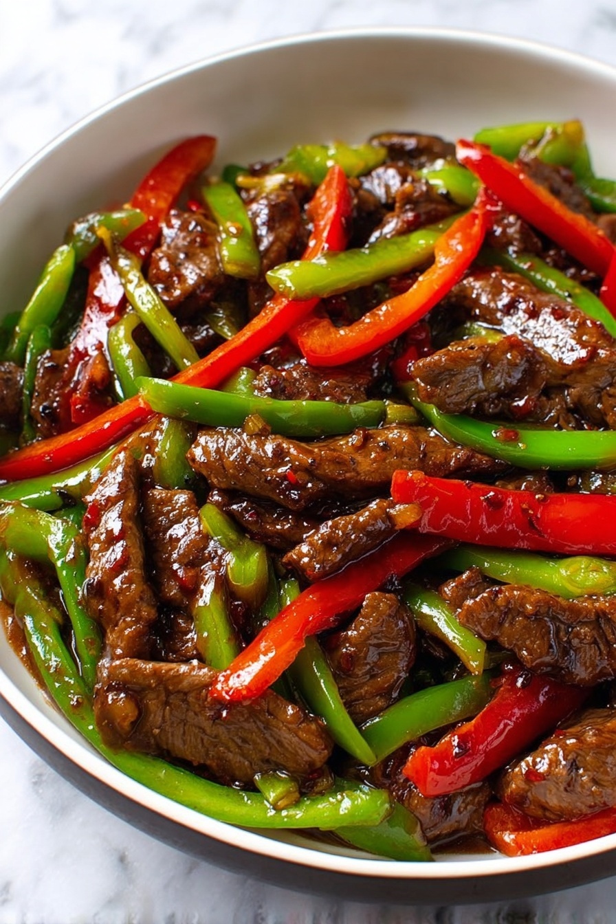 The dish shows several pieces of glossy, dark brown beef slices scattered throughout, coated with a thick shiny sauce. Bright red bell pepper strips and vibrant green bell pepper strips are mixed evenly among the beef pieces, adding a pop of color. The food sits inside a white plate with a black rim, which contrasts with the colorful ingredients. The surface beneath the plate is a white marbled texture. The image captures the fresh, cooked look of the stir-fry with a close-up view, emphasizing the glossy sauce and vibrant vegetable colors. photo taken with an iphone --ar 2:3 --v 7