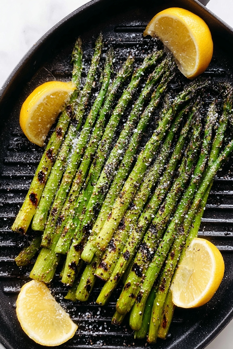A white round grill pan holds one layer of bright green grilled asparagus spears, showing slight char marks in dark brown and black along their length. The asparagus is sprinkled evenly with coarse white salt and cracked black pepper. Three lemon wedges with yellow skin and pale flesh are placed on the side inside the grill pan, also showing some grill marks. The pan rests on a white marbled surface. Photo taken with an iphone --ar 2:3 --v 7