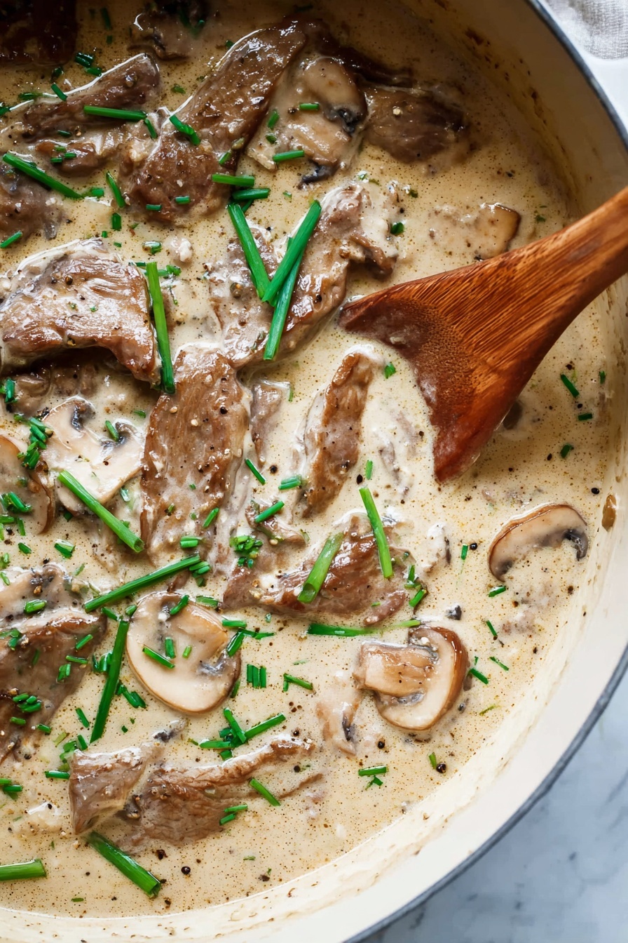 A close-up view of a creamy sauce dish in a dark pan, showing several pieces of browned meat and sliced mushrooms fully covered in light tan sauce with a smooth texture. Small green onion slices are scattered on top, adding bright green spots to the dish. A wooden spoon is partially dipped into the sauce on the right side, its natural wood texture contrasting with the creamy sauce. The white marbled texture surface can be seen around the pan edges. photo taken with an iphone --ar 2:3 --v 7