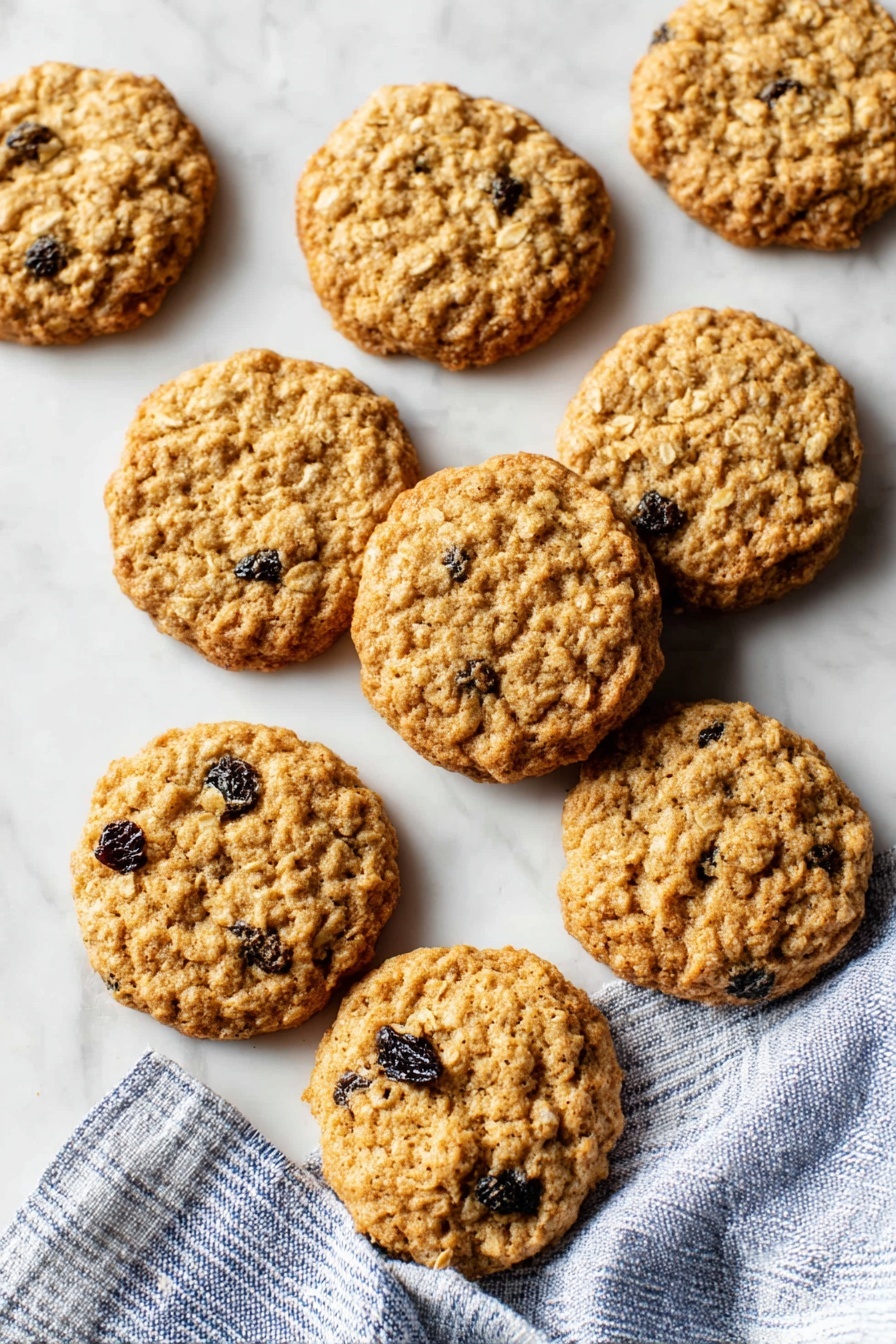 A group of about twenty round oatmeal raisin cookies spread out on a white marbled surface with some overlapping each other, showing a lightly golden brown color with visible bumps from oats and dark spots from raisins inside each cookie, with a crumpled white parchment paper underneath some of the cookies and a folded blue-and-white striped cloth on the right edge, photo taken with an iphone --ar 2:3 --v 7